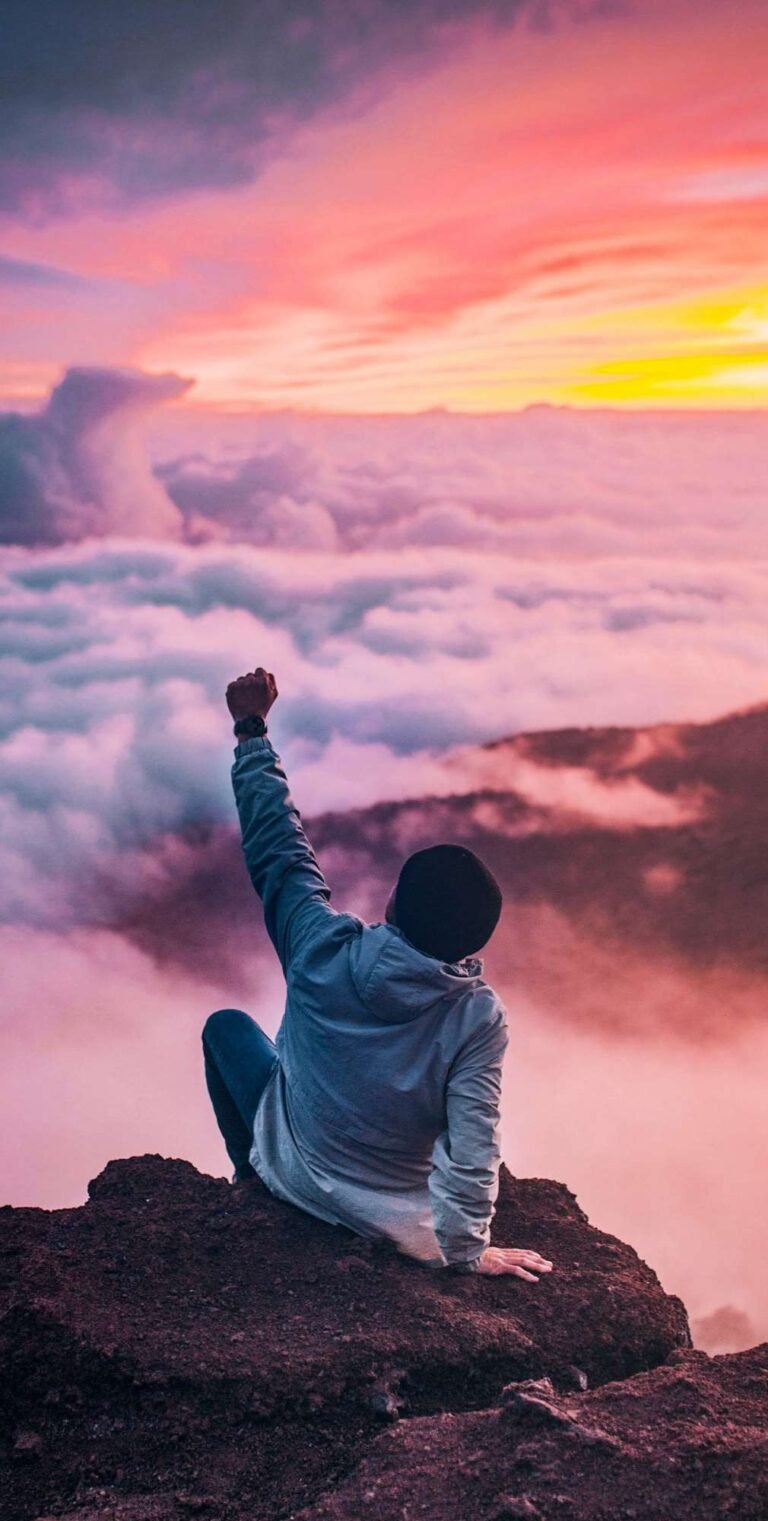 man sitting on mountain top celebrating healing succcess
