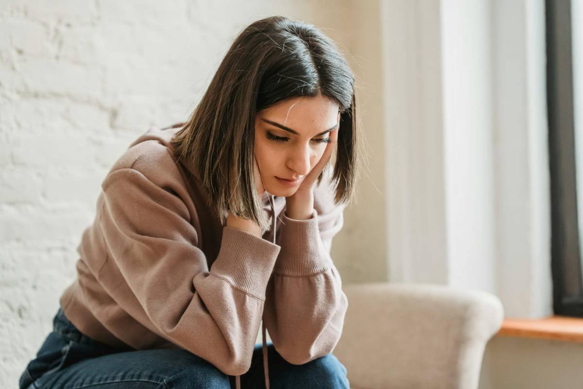 Woman experiencing anxiety. Looking downwards with both hands on her face.