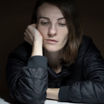 Woman experiencing depression with hand on her face looking downwards.